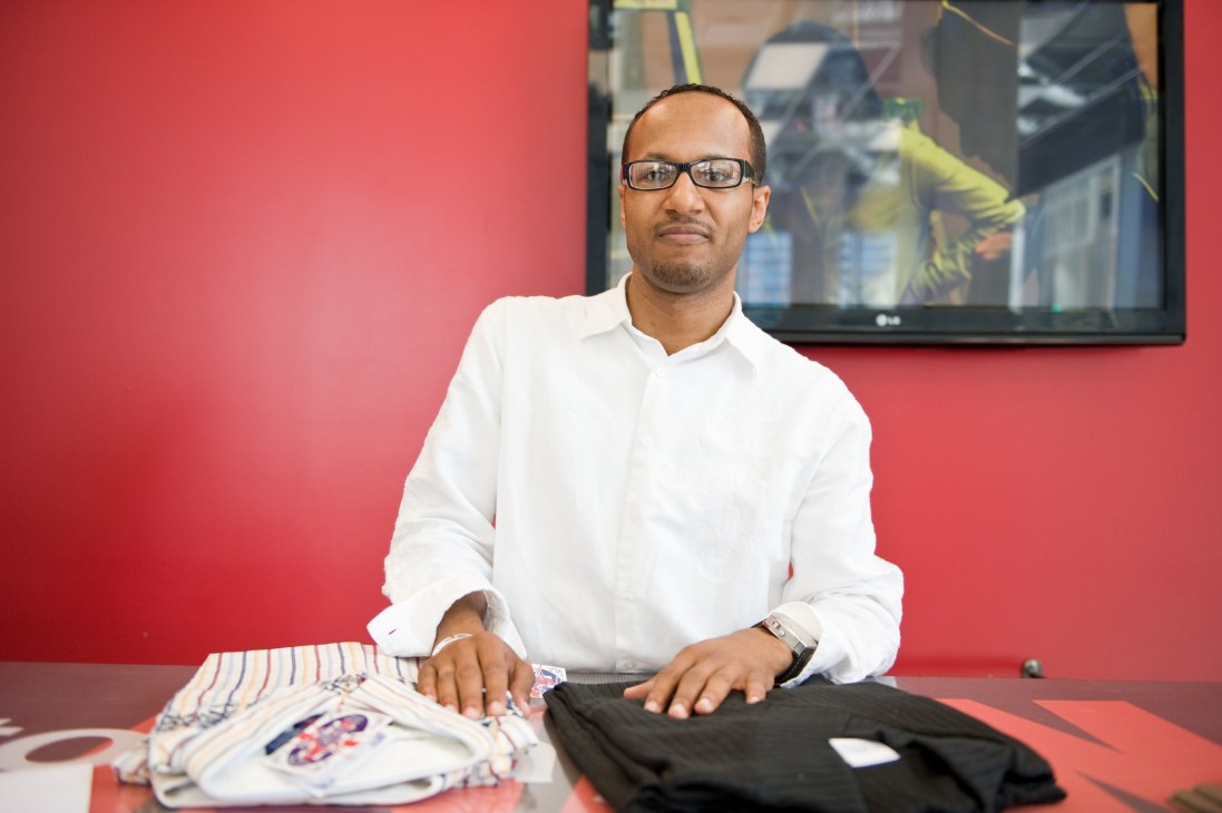 Entourage Man owner Willie Davis sits at a desk against a red wall wearing a white shirt and glasses.