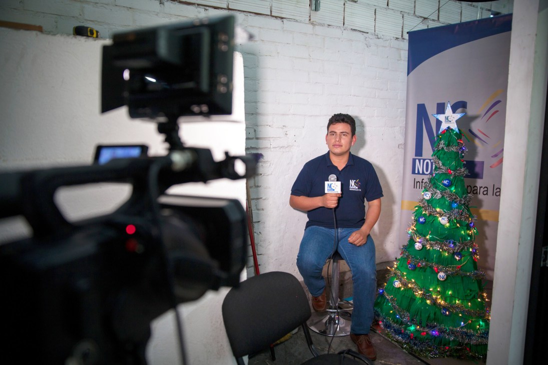 Former Farc militant in NC Noticias studio holds microphone while being filmed, with Christmas tree backdrop.