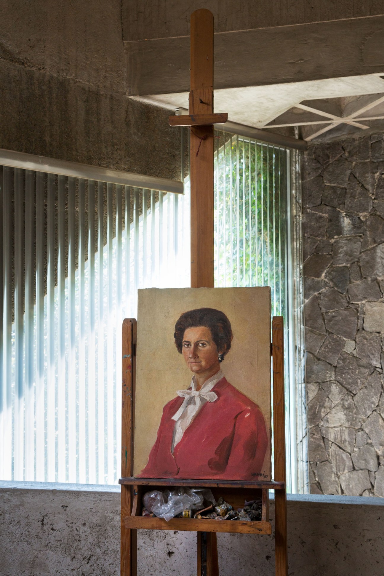 Portrait painting of a woman in a red jacket with white collar on an easel in a concrete interior