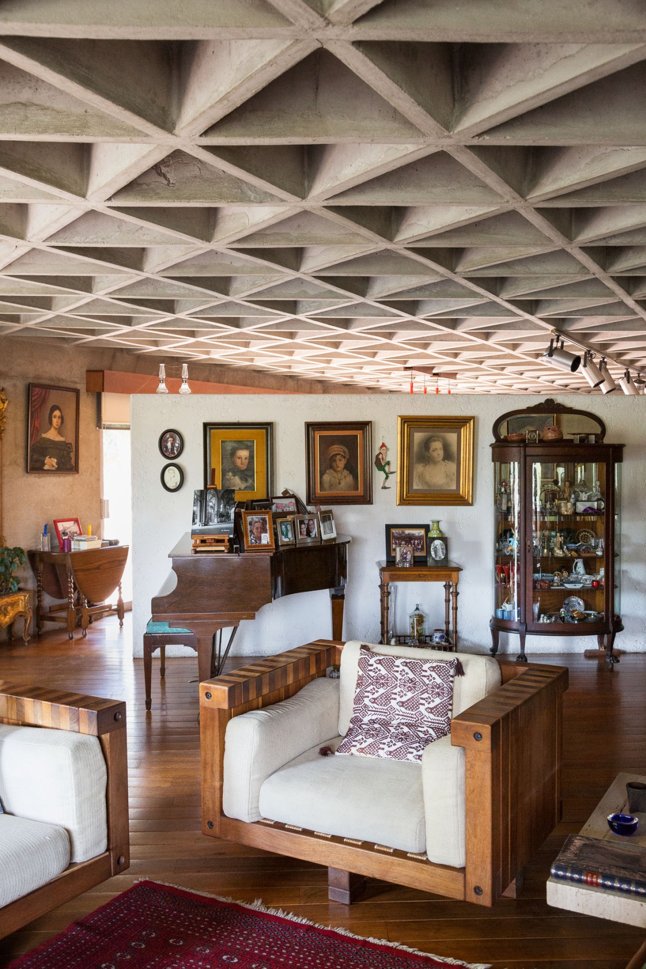 Interior living room with wooden sofas designed by Gallardo, featuring a distinctive triangular hollow concrete ceiling and family portraits.