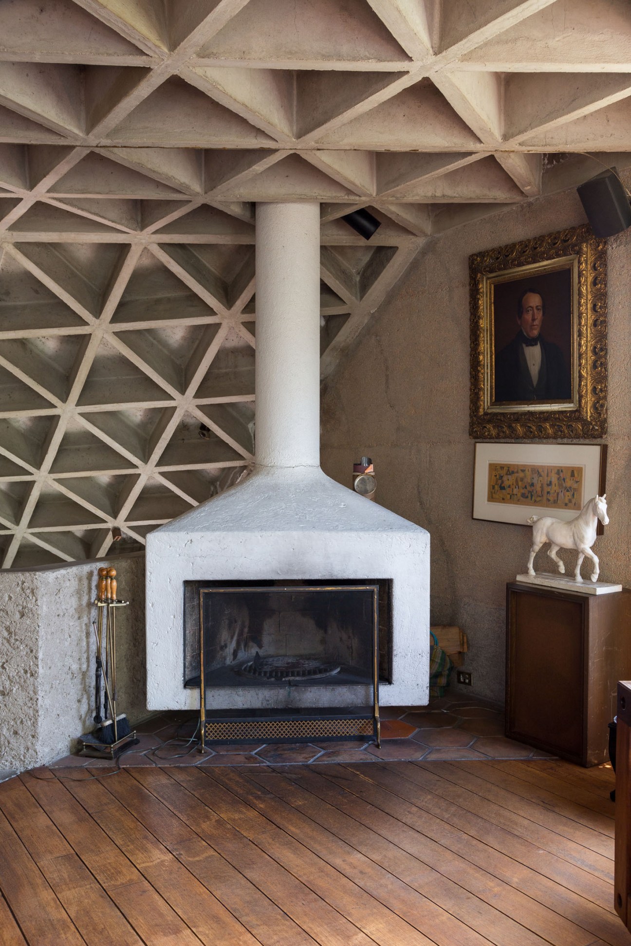 Interior of modernist home with triangular patterned concrete ceiling, white fireplace, and artworks on walls.