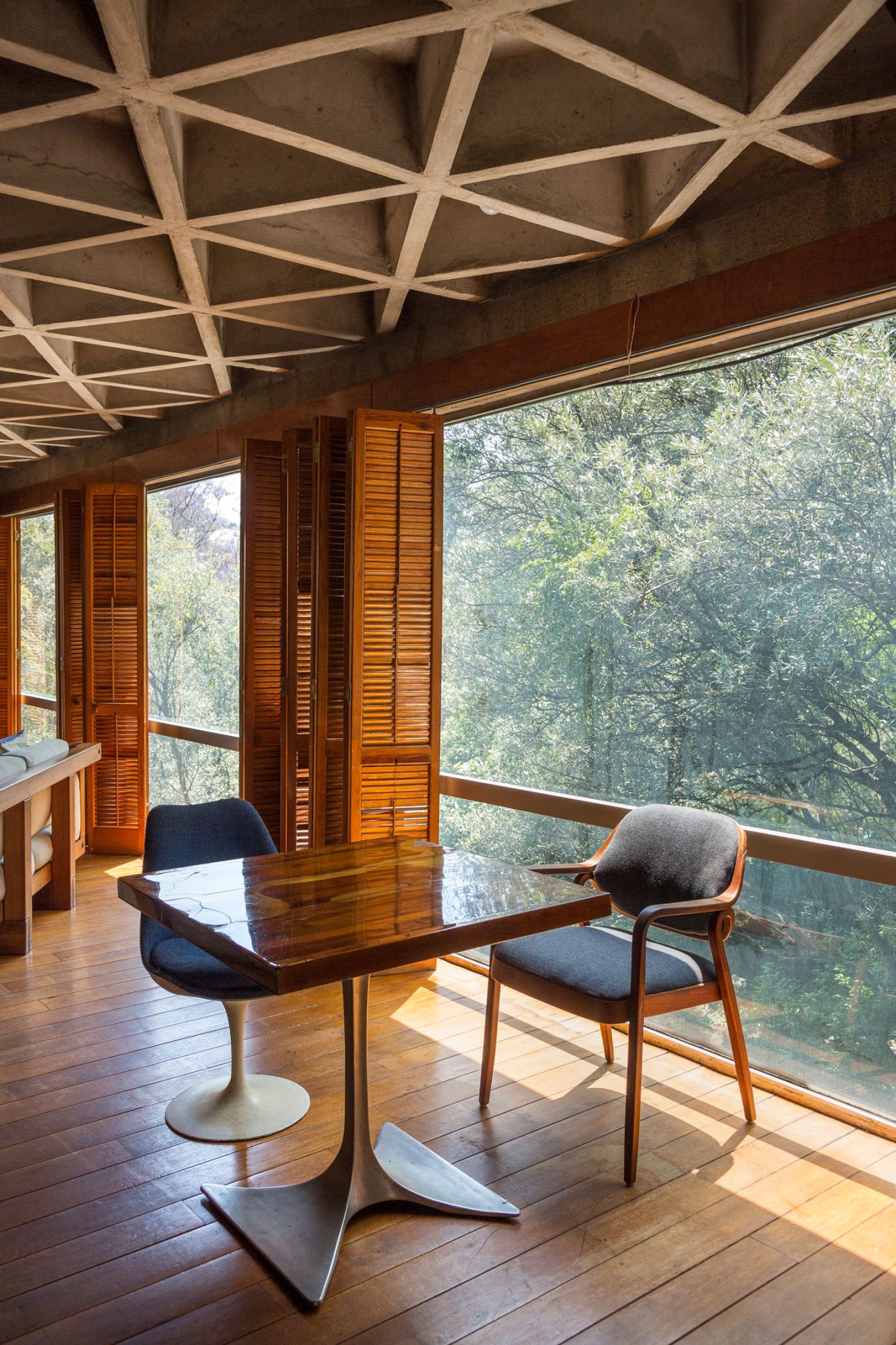 Mid-century modern workspace with HemisFair 68 table and chair designed by Ernesto Gallardo, featuring concrete ceiling and forest views.