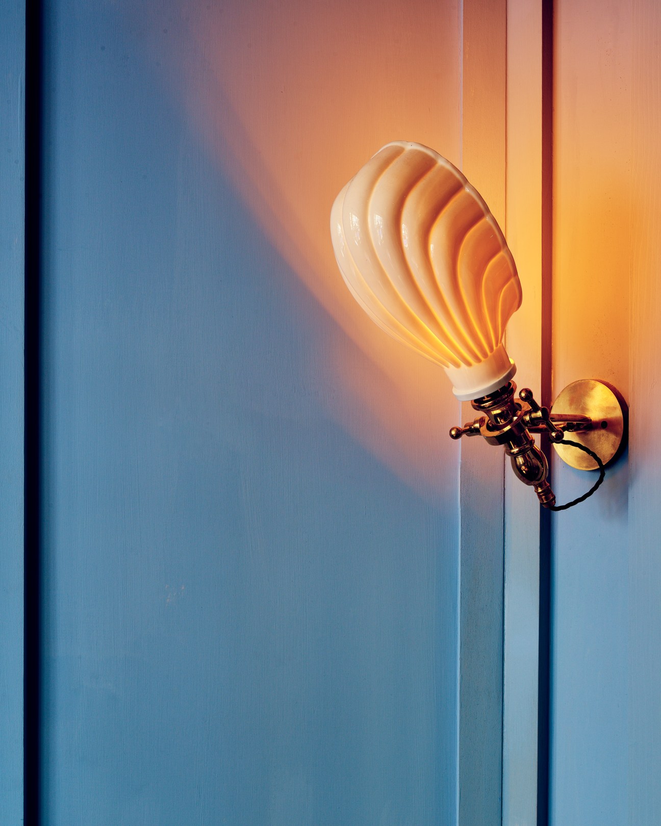 Illuminated shell-shaped sconce with warm amber glow mounted on teal wall.