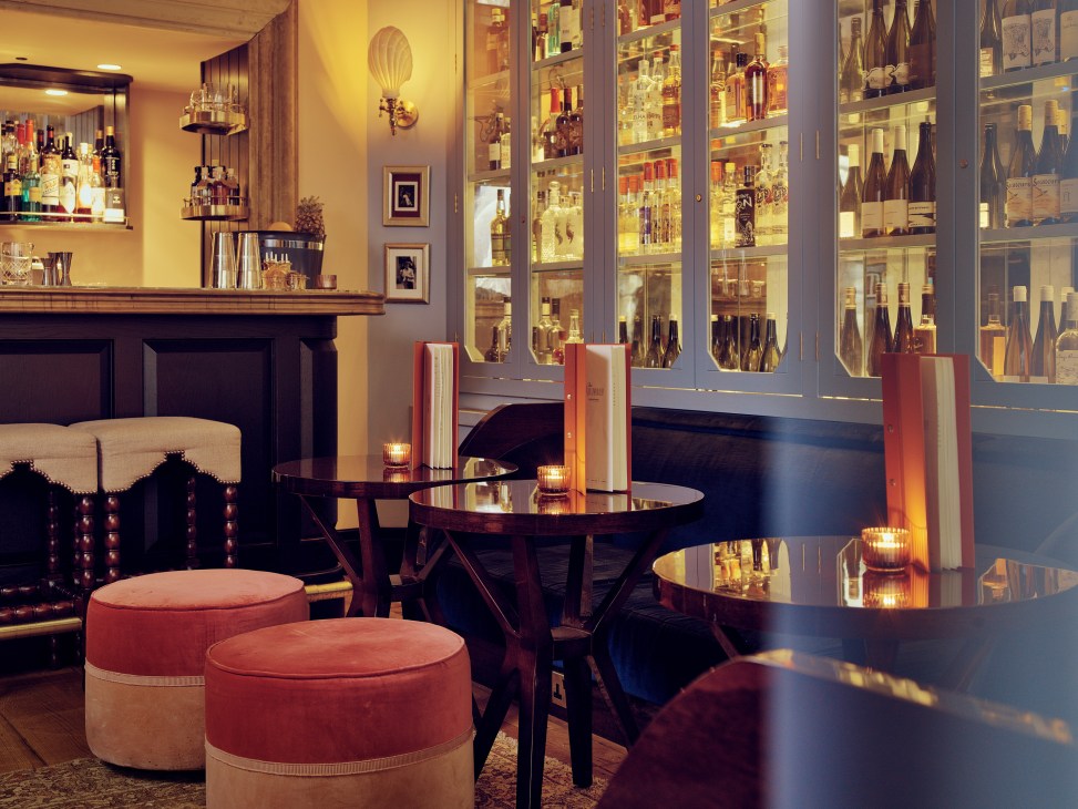 The Mulwray cocktail bar with red velvet banquettes, round tables, and illuminated glass spirit cabinets.