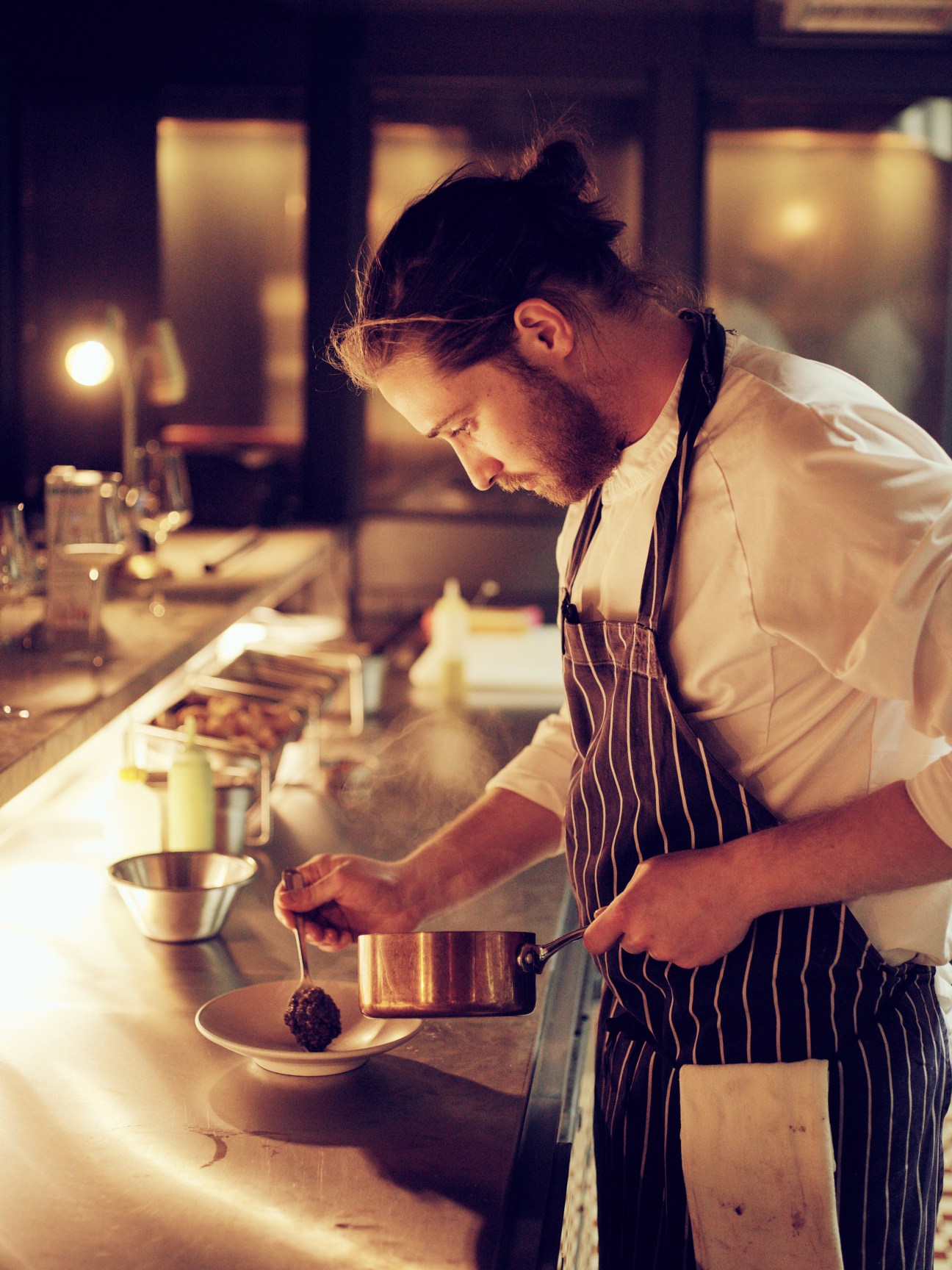 Chef plating a dish at Evelyn's Table counter in moody lighting.