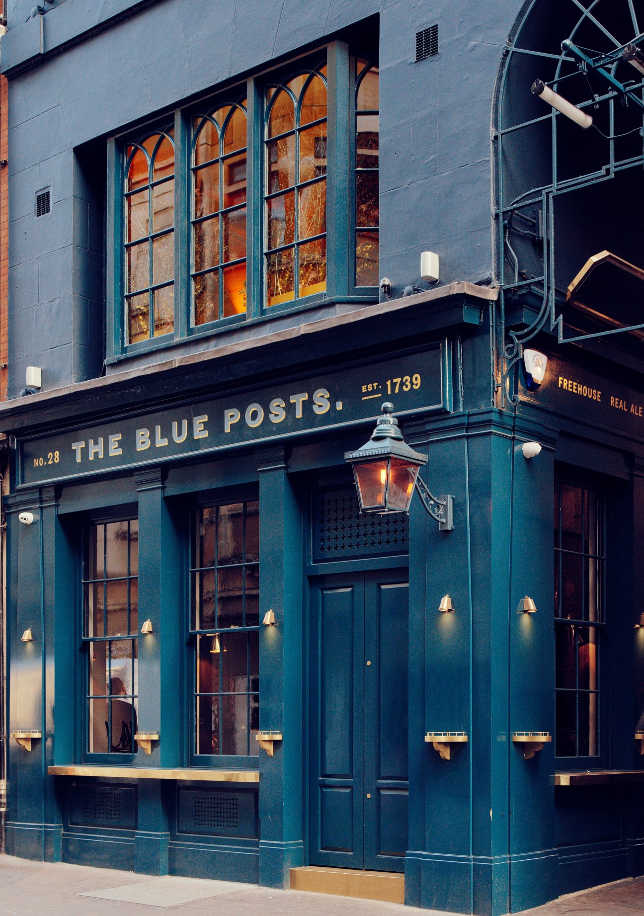 The Blue Posts pub exterior with teal-painted facade, brass fixtures, and large windows showing establishment date 1739.