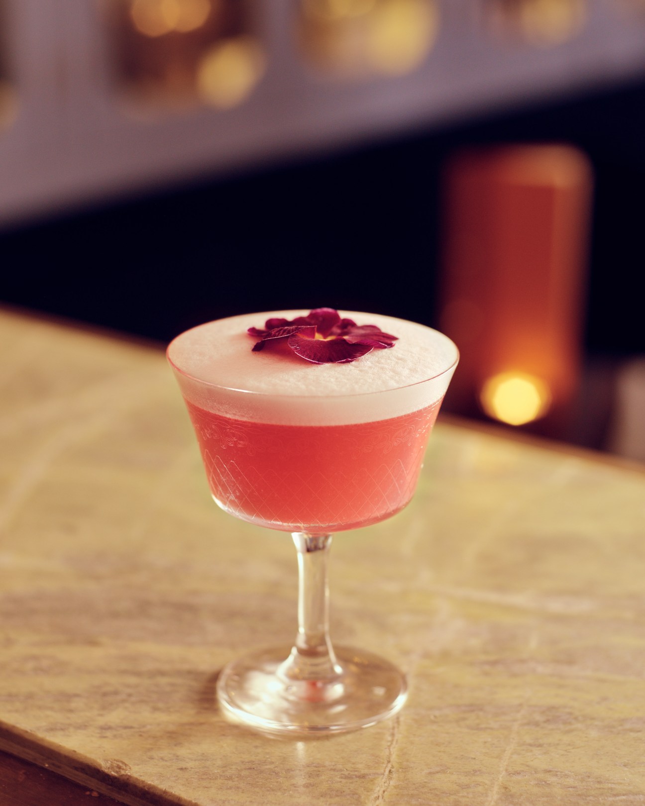 A pink cocktail with white foam top and rose petal garnish in a coupe glass at The Blue Posts bar.
