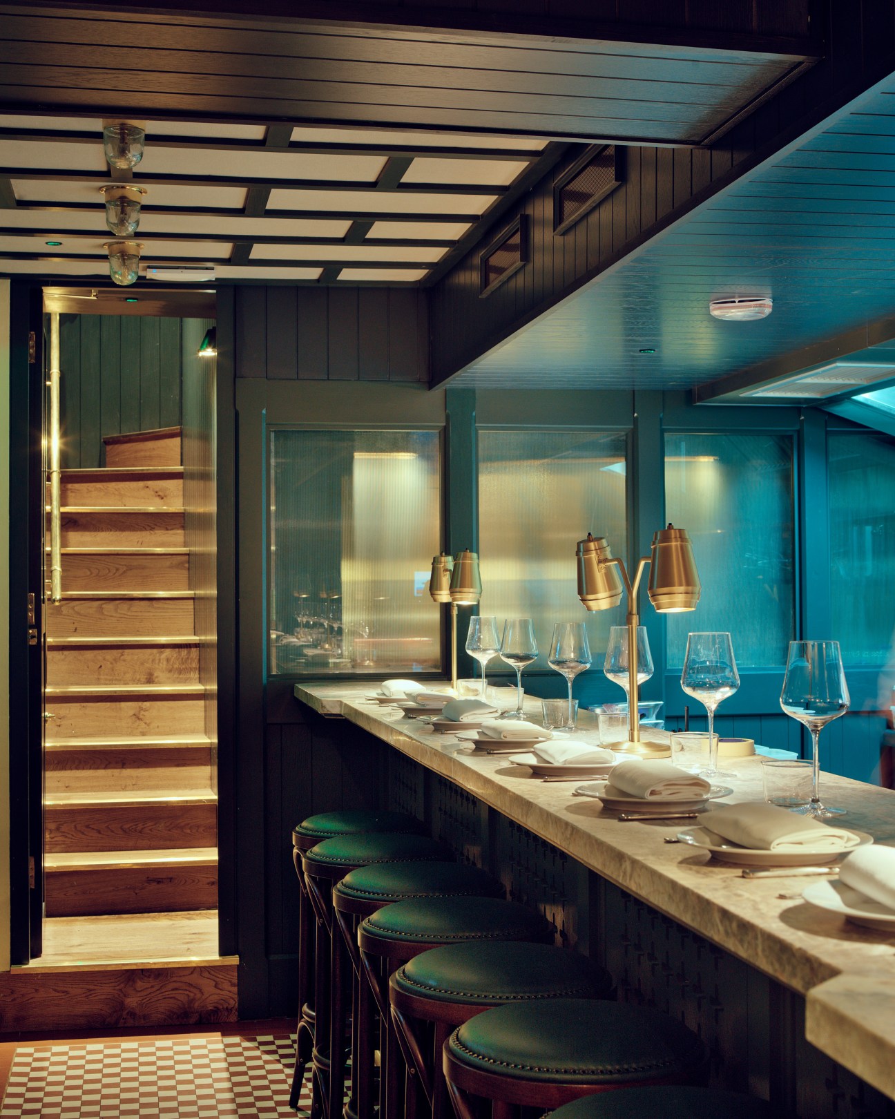 Evelyn's Table restaurant counter with green leather barstools, place settings, and hanging brass pendant lights.