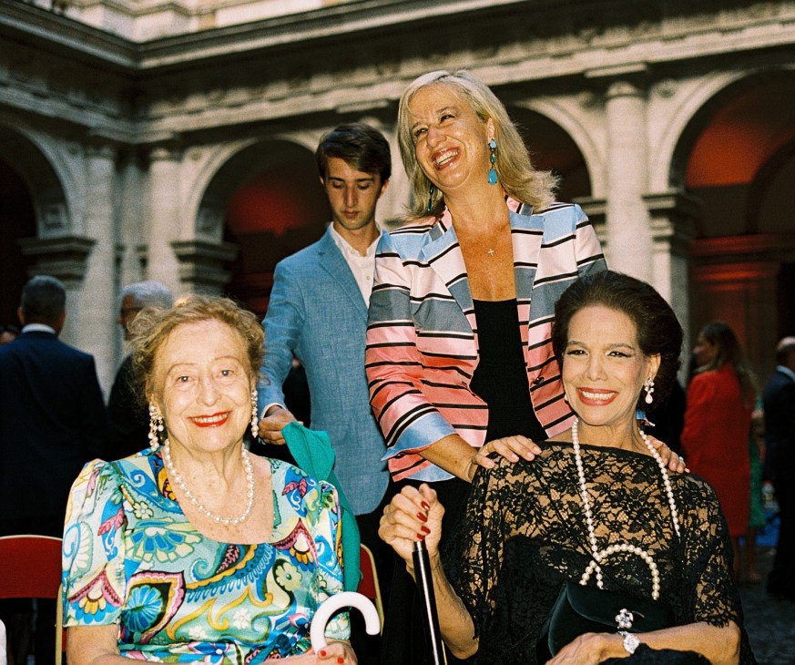 Three elegantly dressed women at a diplomatic reception at Palazzo Farnese in Rome.