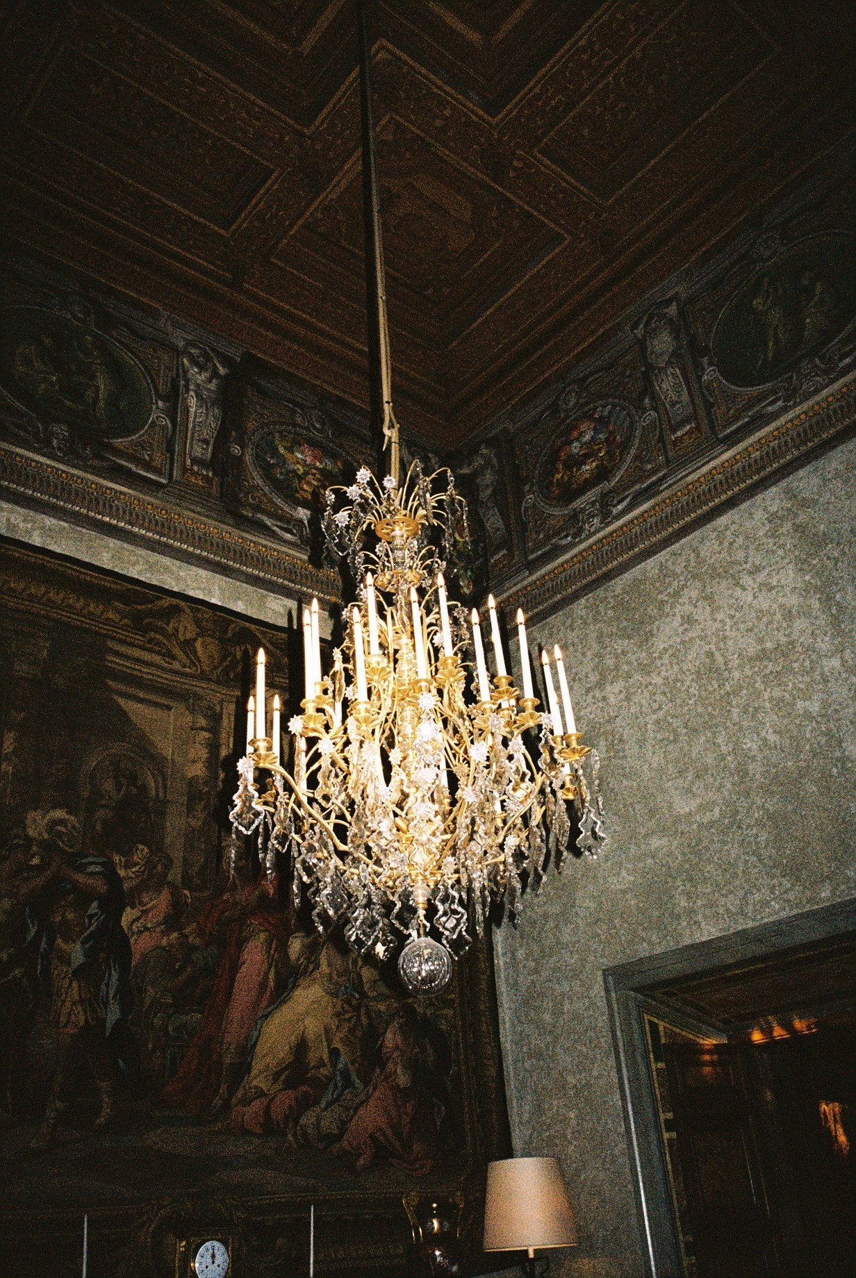 Ornate crystal chandelier hanging in an elegantly decorated room with frescoed ceiling and detailed wall panels at Palazzo Farnese.