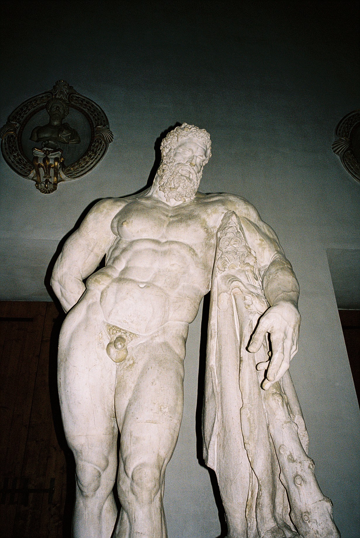 White marble classical male statue with curly beard and draped robe displayed in gallery setting