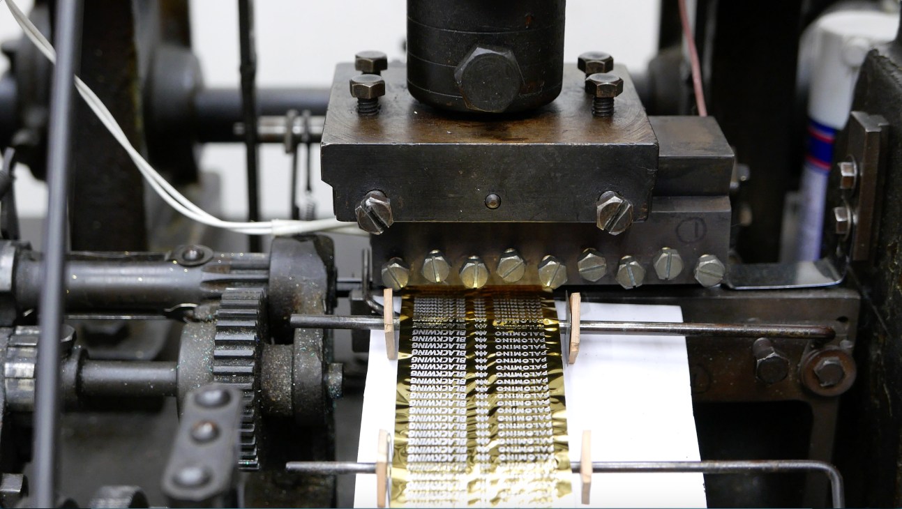 Industrial pencil logo printing machine with metal clamp pressing gold foil onto wooden pencil bodies on production line.