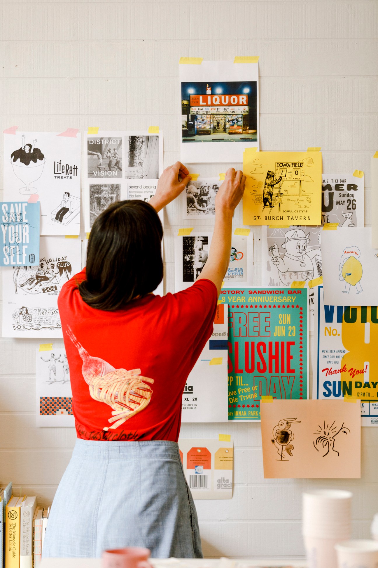 Person in red shirt arranging design materials and posters on white wall at Family Brothers studio