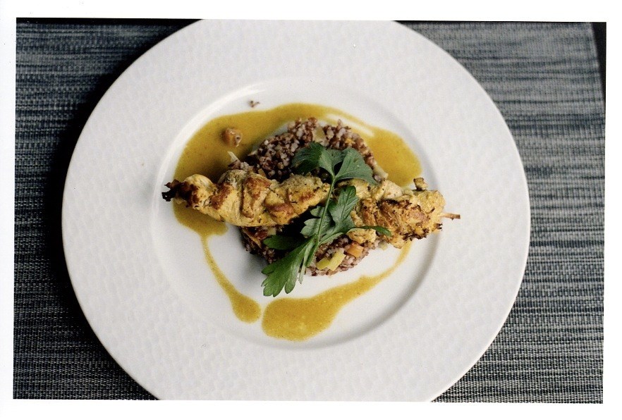 Brochette de volaille chicken kebab with spiced sauce, rice and herbs on white plate.