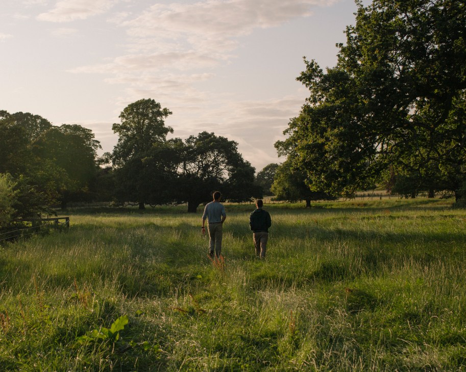 Two people jogging through grassy fields at Balcaskie estate with mature trees in the background.