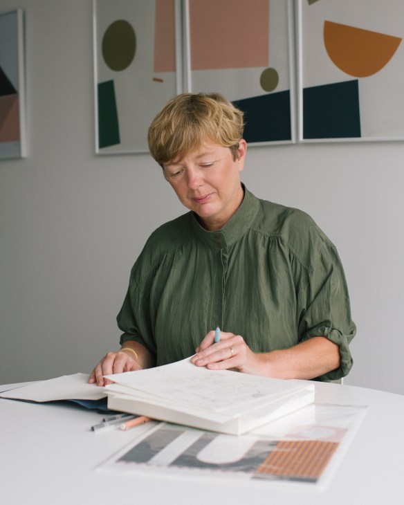 Kirsty Thomas of graphic studio Tom Pigeon reviewing design work at a table with color swatches and sketches.