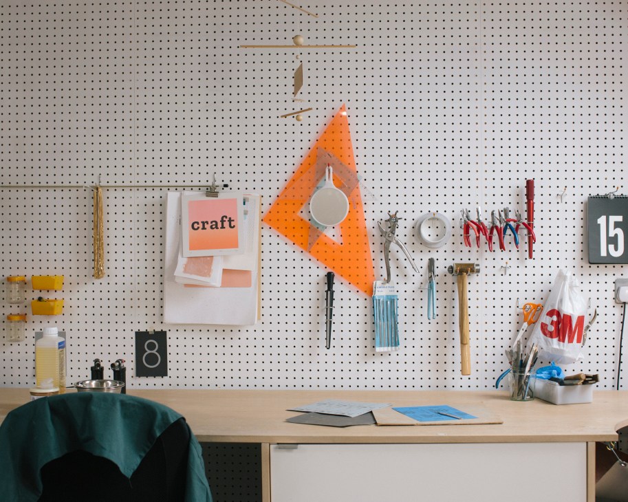 Tom Pigeon's graphic design studio workspace with pegboard wall displaying craft supplies, tools, and design samples.
