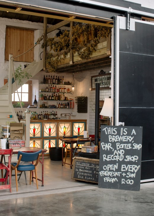 Interior of East Neuk Organic Brewing & Distilling storefront with bottles displayed on shelves and stained glass windows.