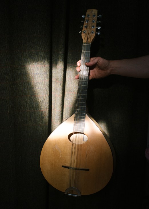 Hand holding wooden mandolin with narrow neck and round body against dark background