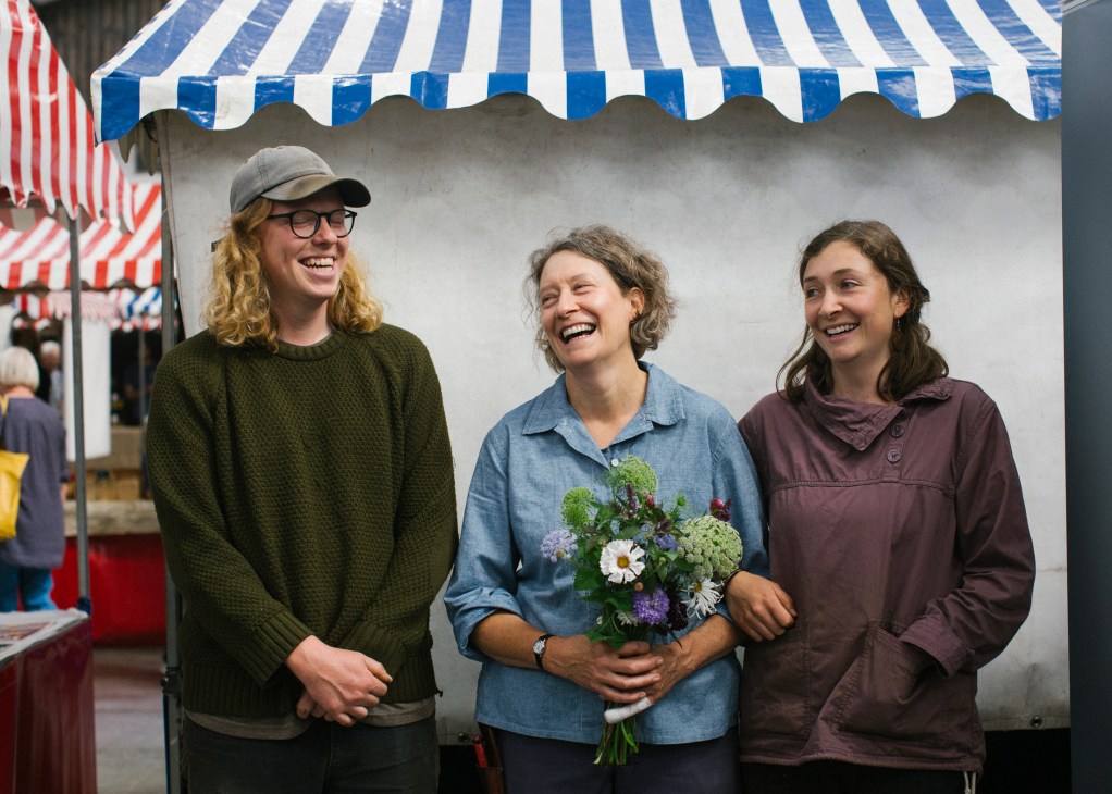 Sarah Hunter of Keeping the Plot holds a flower bouquet with her daughter Connie and husband Tom Booth at a market stall.
