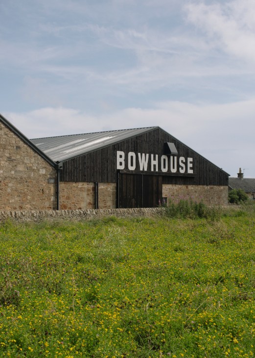 Modern black corrugated metal barn with white Bowhouse signage surrounded by wildflower meadow.