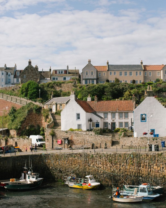 Crail Harbour in the East Neuk of Fife with fishing boats moored below stone walls and historic buildings on the hillside.