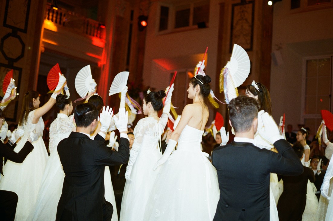 Debutantes in white ball gowns holding white fans during a traditional Viennese ball performance