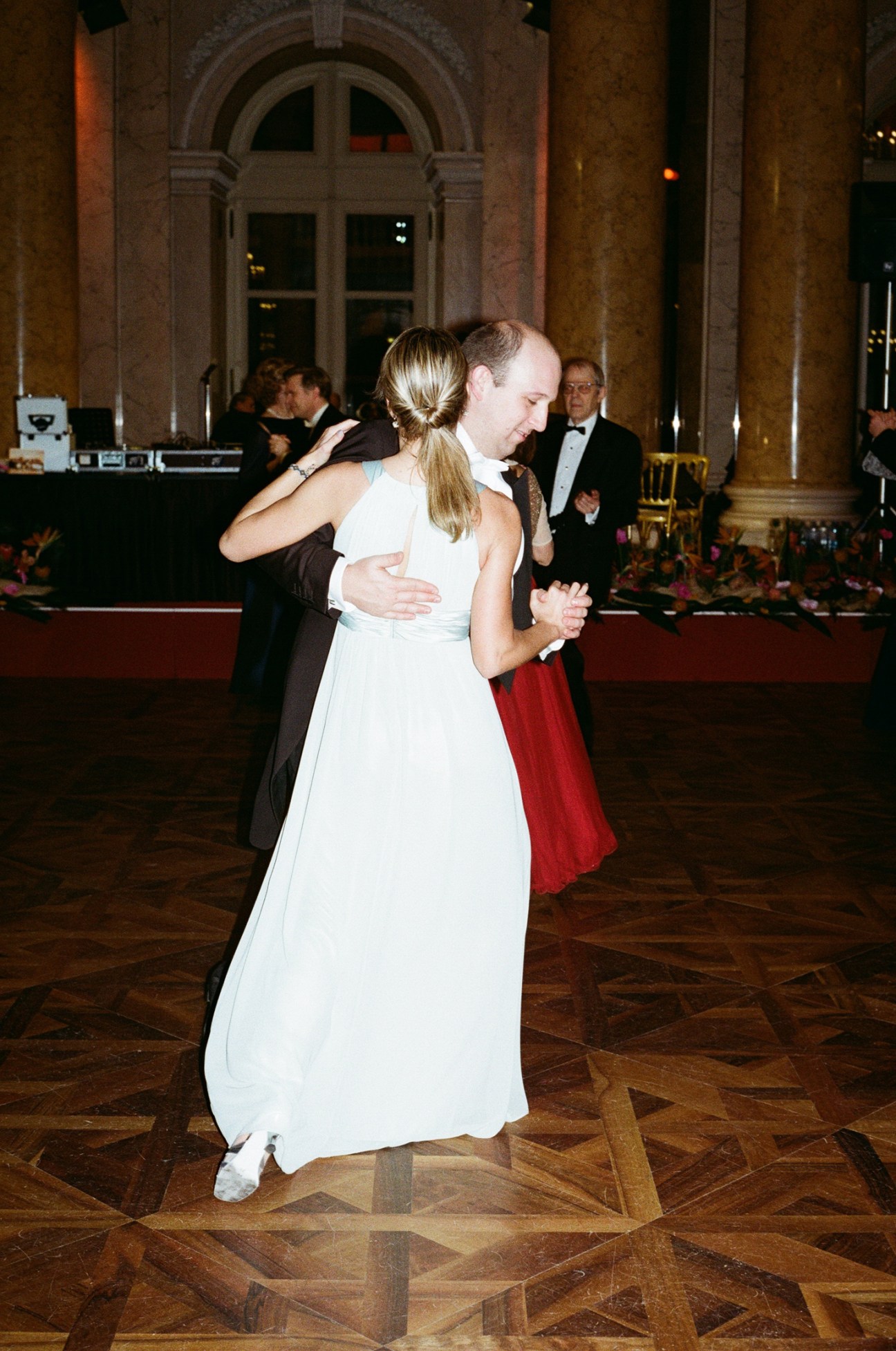 A couple in formal attire dancing waltz in an ornate ballroom with parquet floors and classical architecture