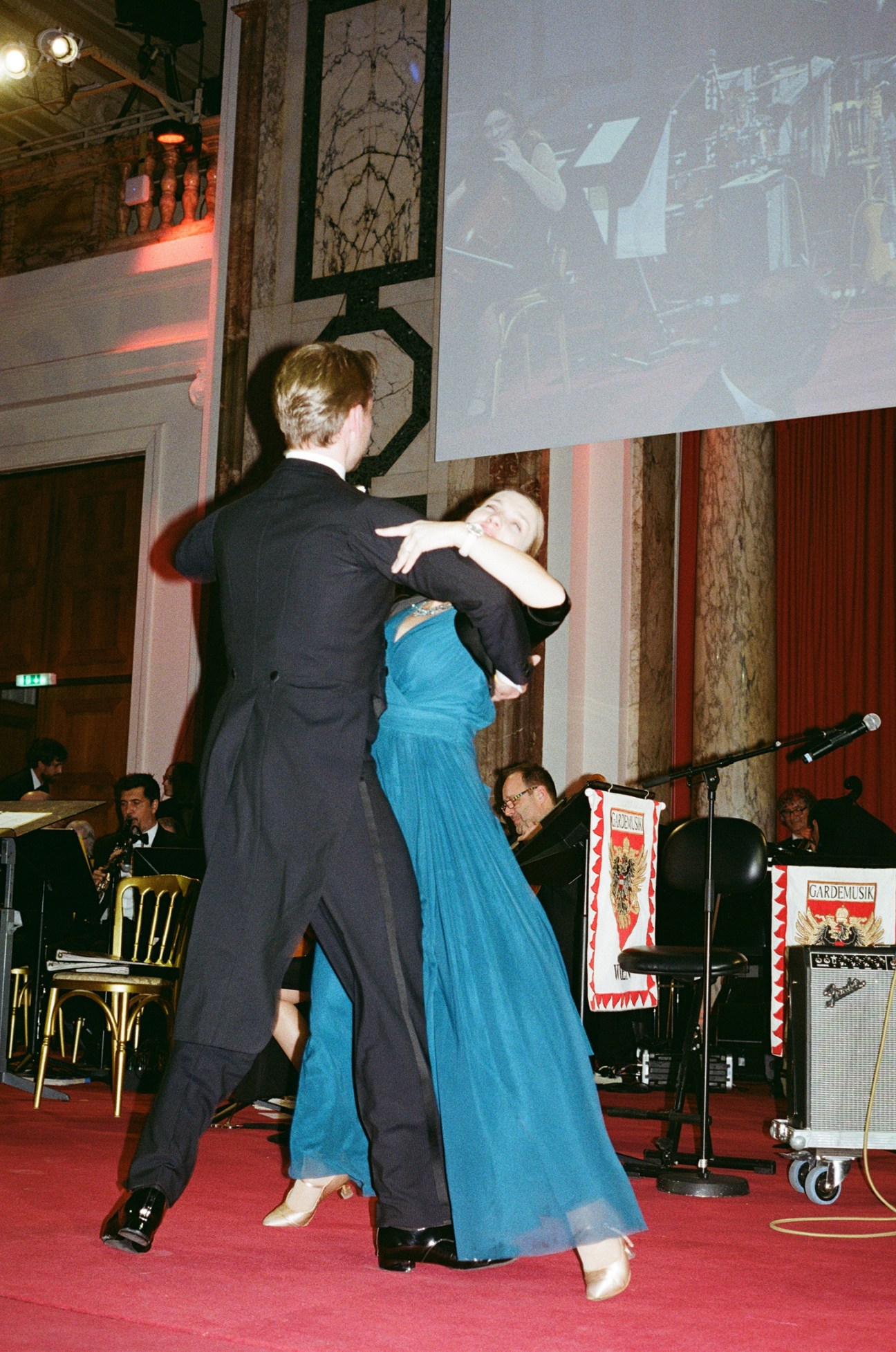 Two people dancing at a formal Viennese ball, with the woman in a blue gown and man in a dark suit