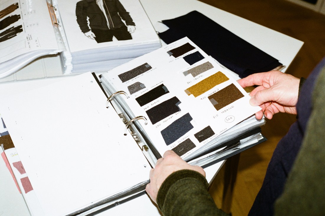 Hands examining fabric swatches in a ring binder with color samples on white pages
