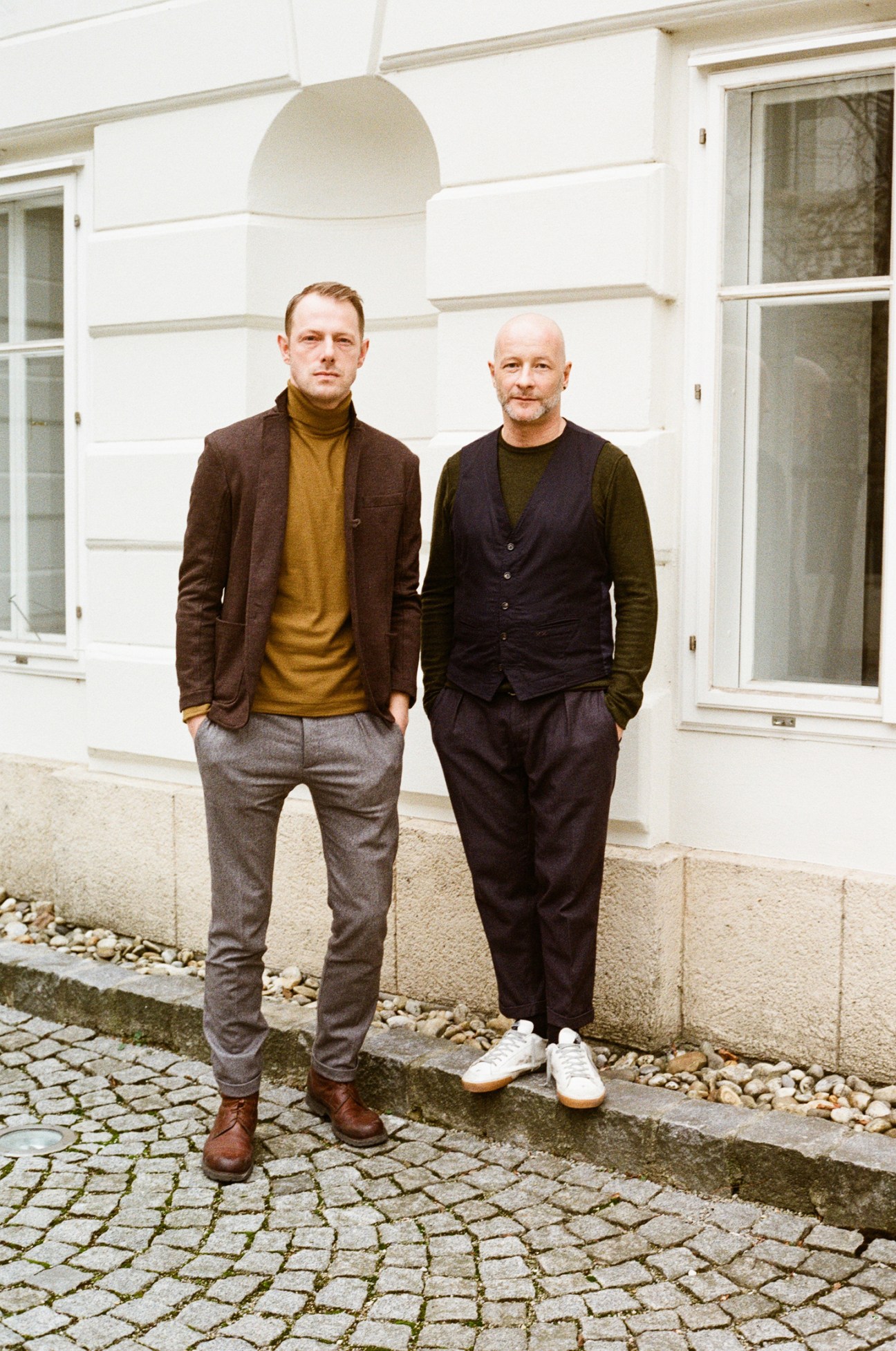 Manuel and Christian Weber standing in front of white baroque building wearing tailored jackets