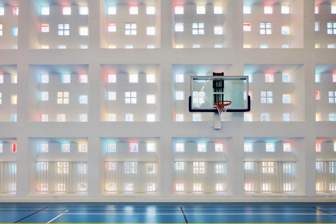 Basketball hoop in a gymnasium with a colorful south-facing facade featuring 650 brightly colored windows providing natural mottled light.