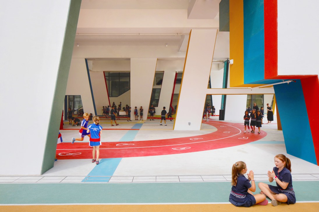 Students play and gather in a bright, colorful undercover playground with multicolored columns and running track.