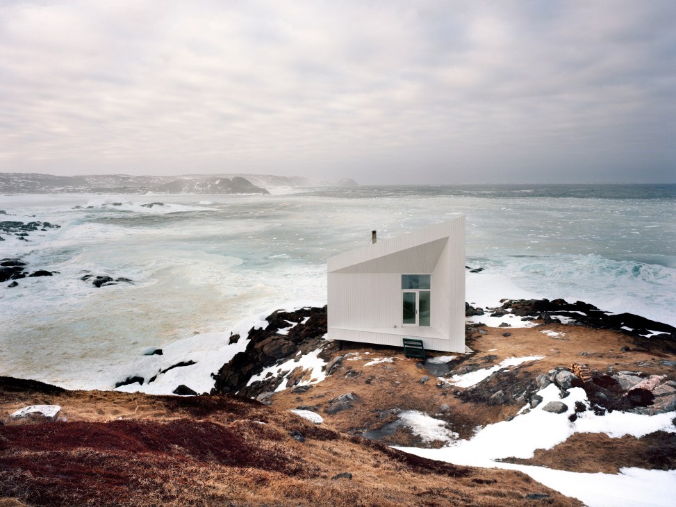 White modernist studio building on rocky Fogo Island coastline overlooking Atlantic Ocean.