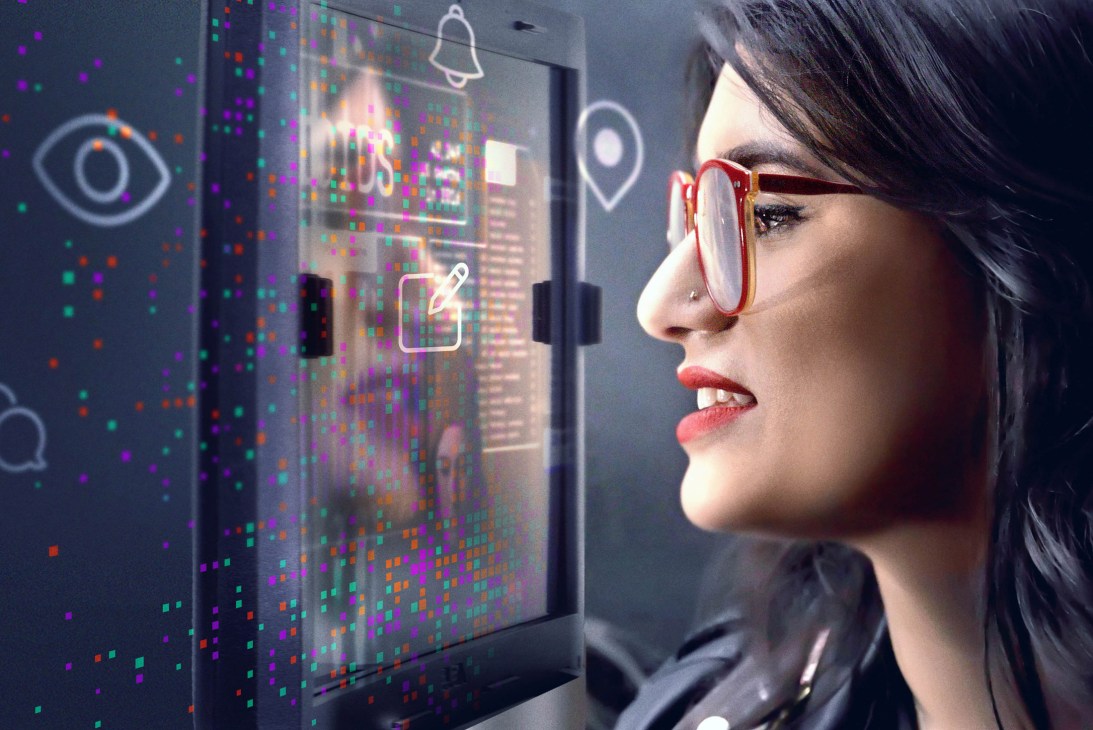 Woman wearing red-framed glasses looking at a digital display showing social media icons and pixelated graphics.