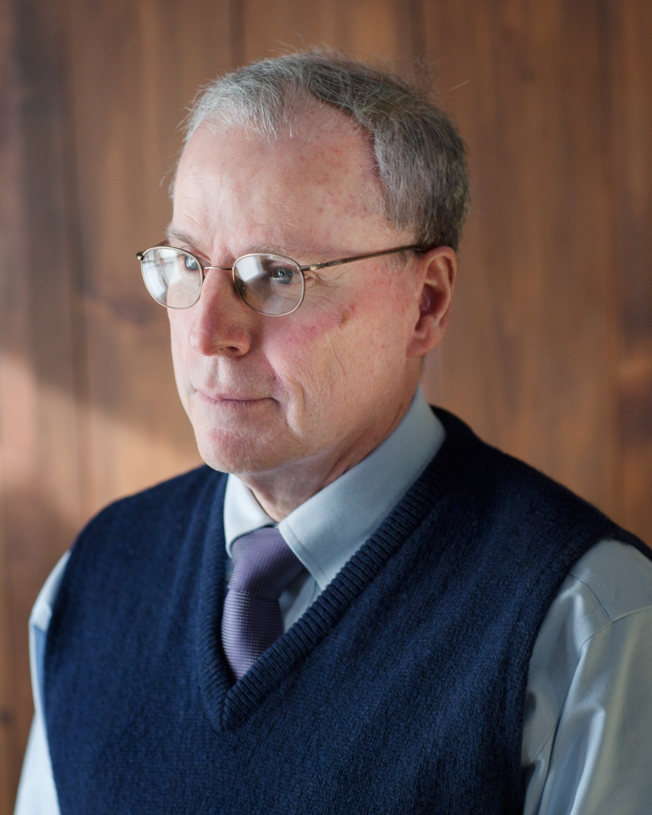Portrait of Robert S Ford, former US ambassador to Syria, wearing glasses and a dark vest over a light blue shirt with purple tie.