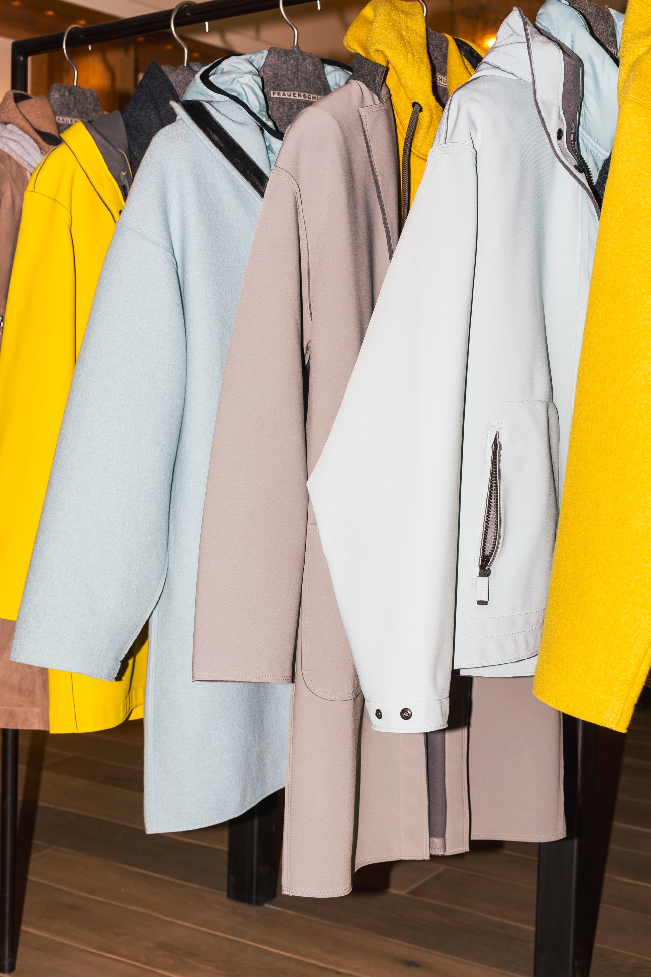 Colorful waterproof jackets hanging on a clothing rack including yellow, light blue, beige and white coats