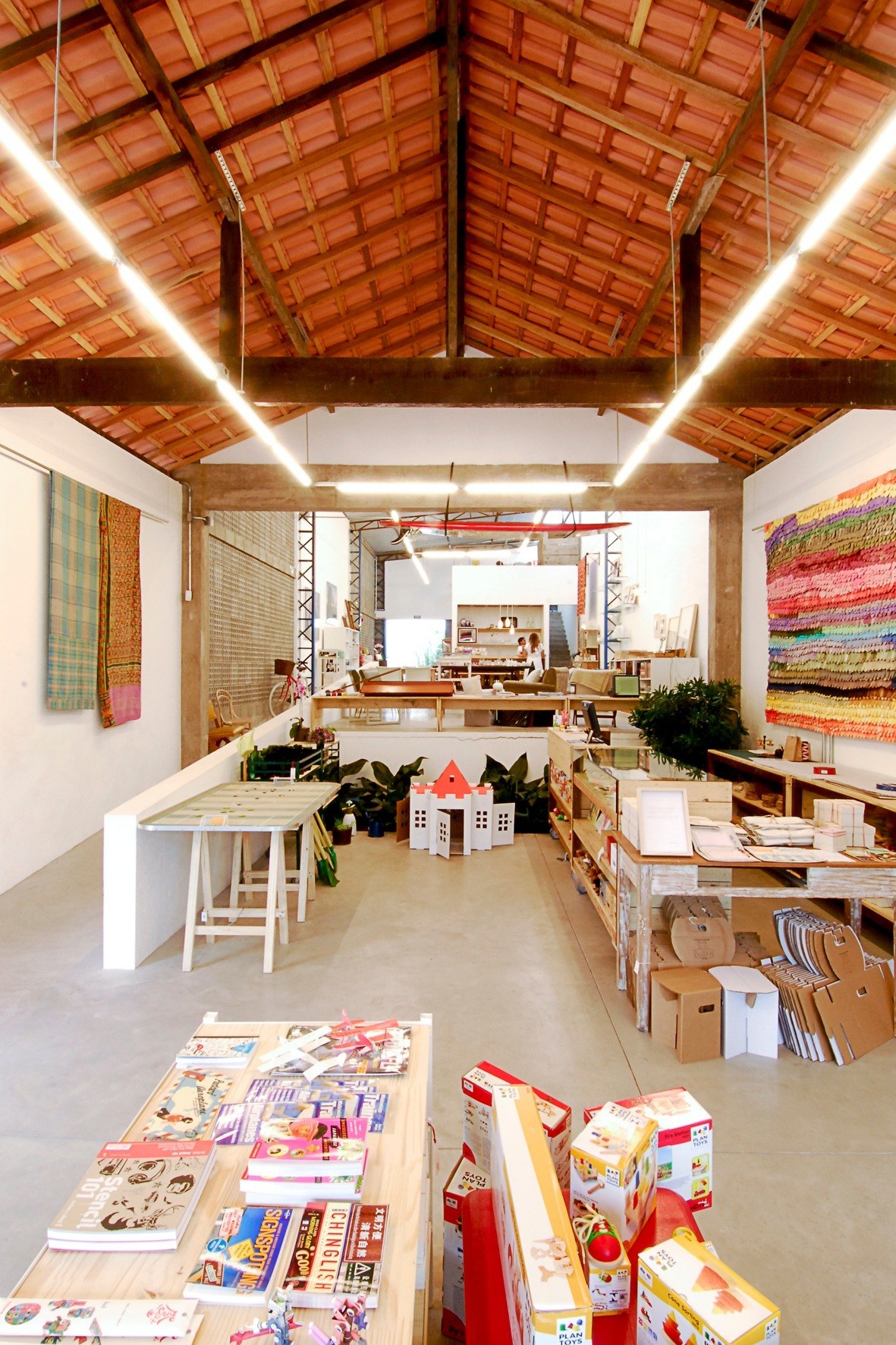 Interior of Amoreira shop in São Paulo showing concrete floors, exposed wooden ceiling beams, and display tables with products.