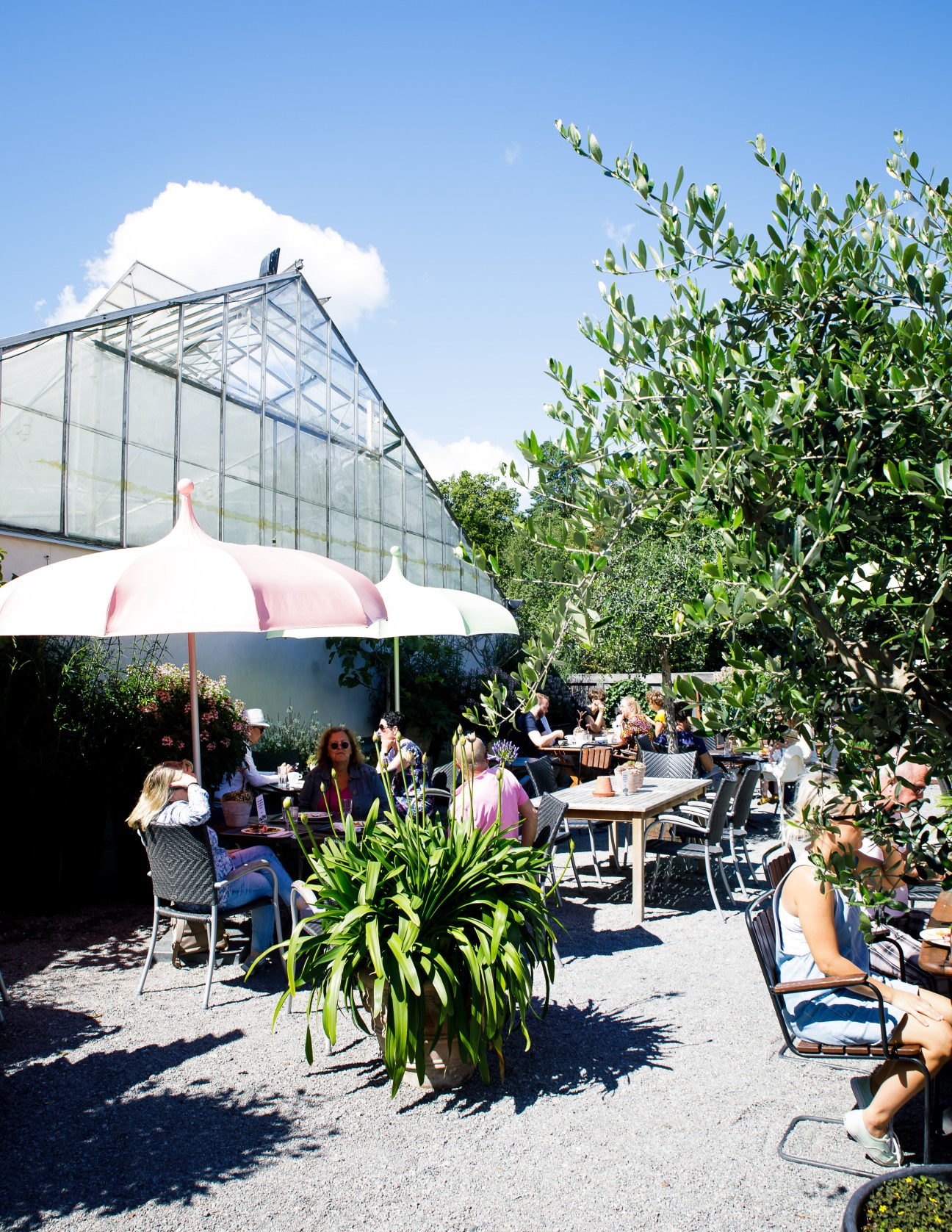 Outdoor dining terrace at Slottsträdgården with customers seated at tables under umbrellas surrounded by lush greenery