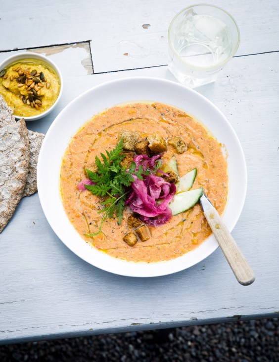 Tomato gazpacho soup with pickled onions, herbs, croutons and cucumber garnish served in a white bowl