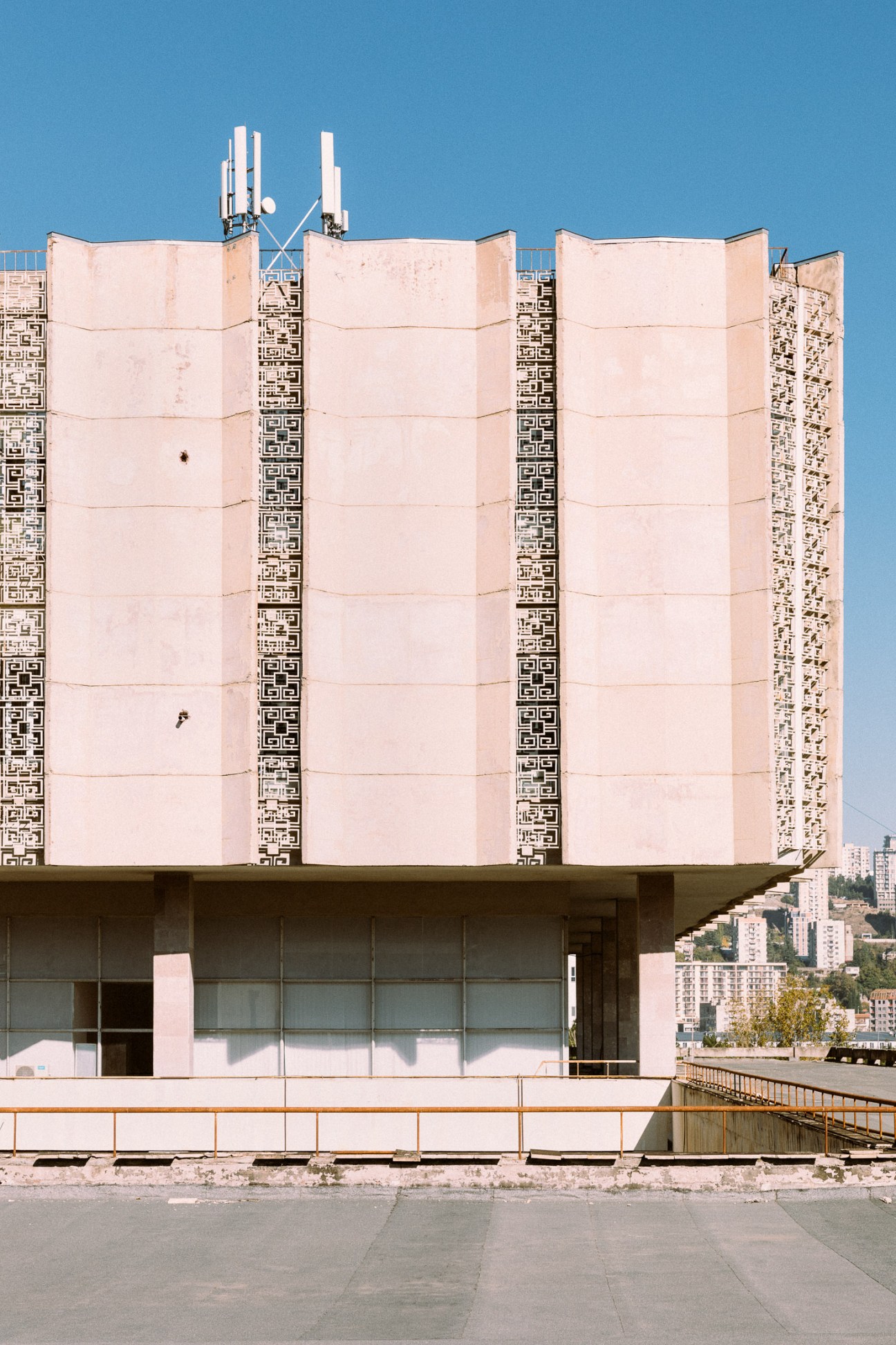 Tbilisi State University's Central Library, a pink brutalist building with geometric patterned facades and cellular antenna on top against blue sky.