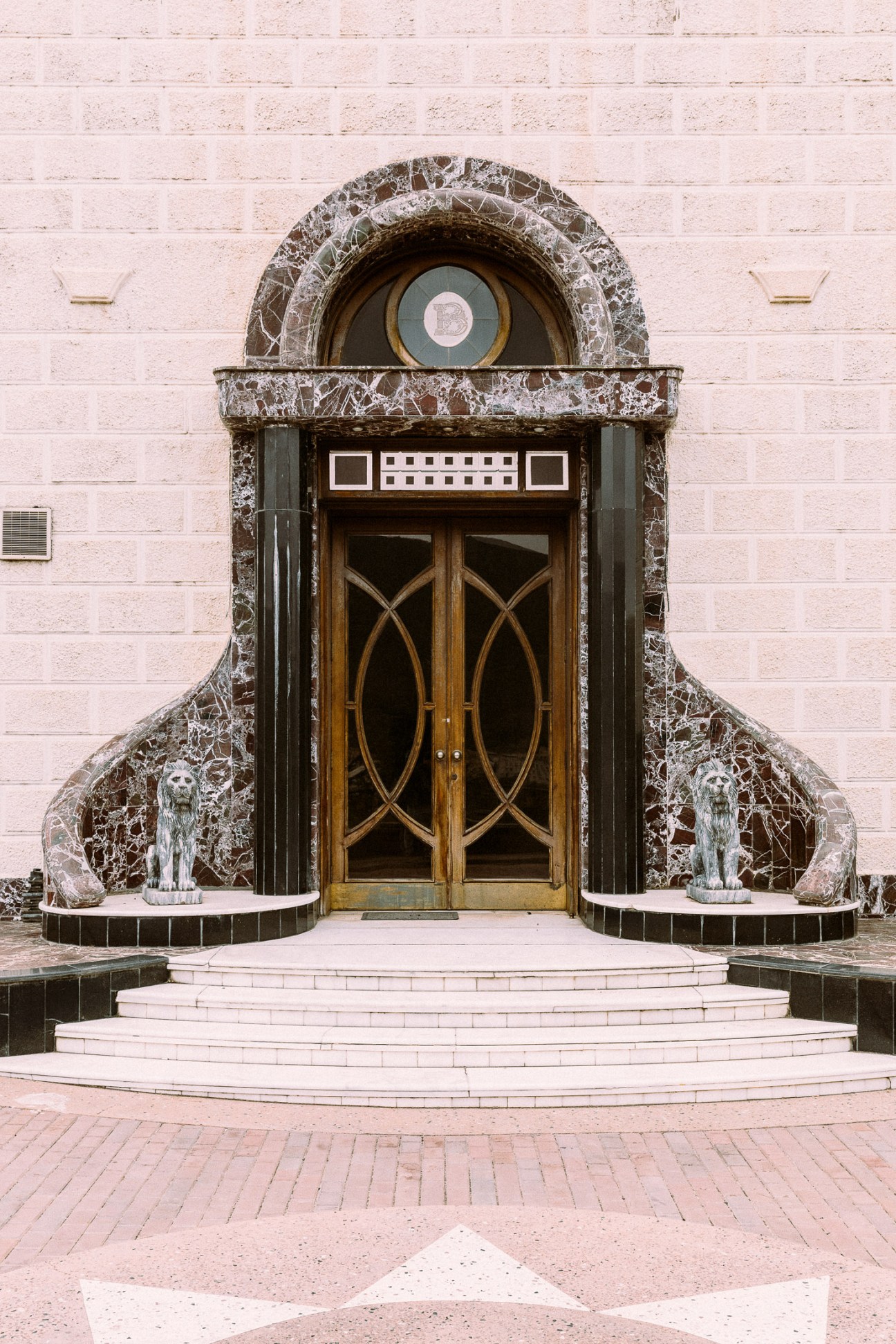 Ornate entrance with arched doorway, marble columns, and two lion statues flanking steps