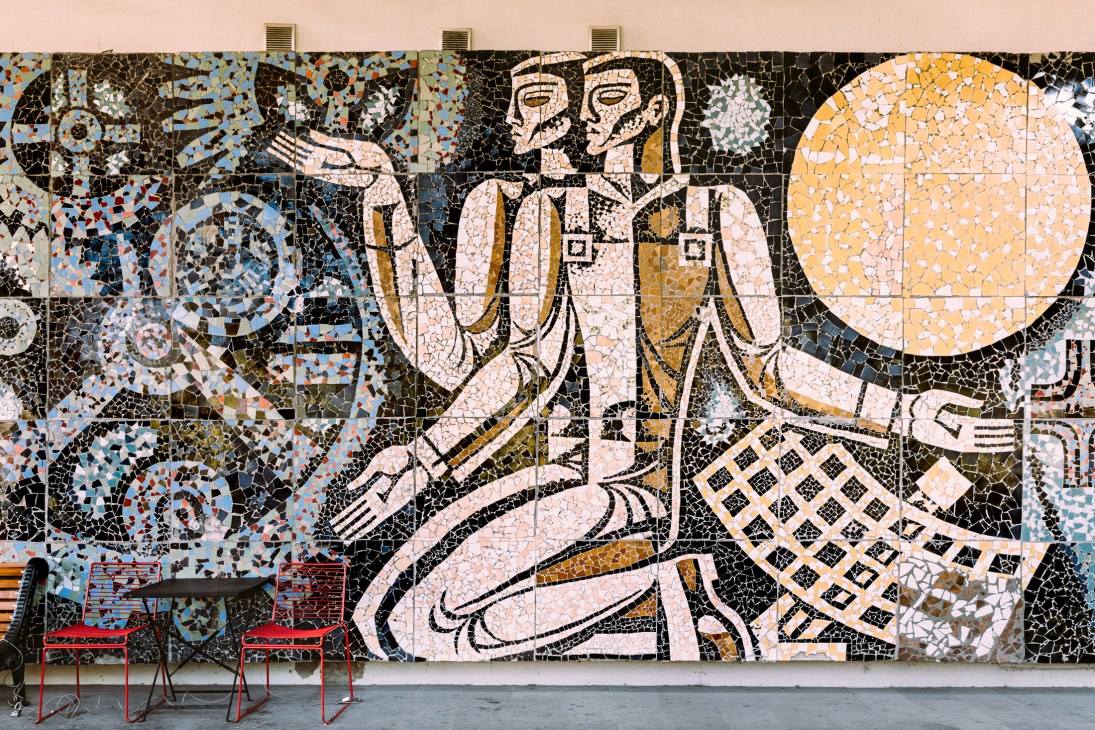 ExpoGeorgia mosaic mural featuring two figures and celestial imagery in colorful tile work with red chairs below.