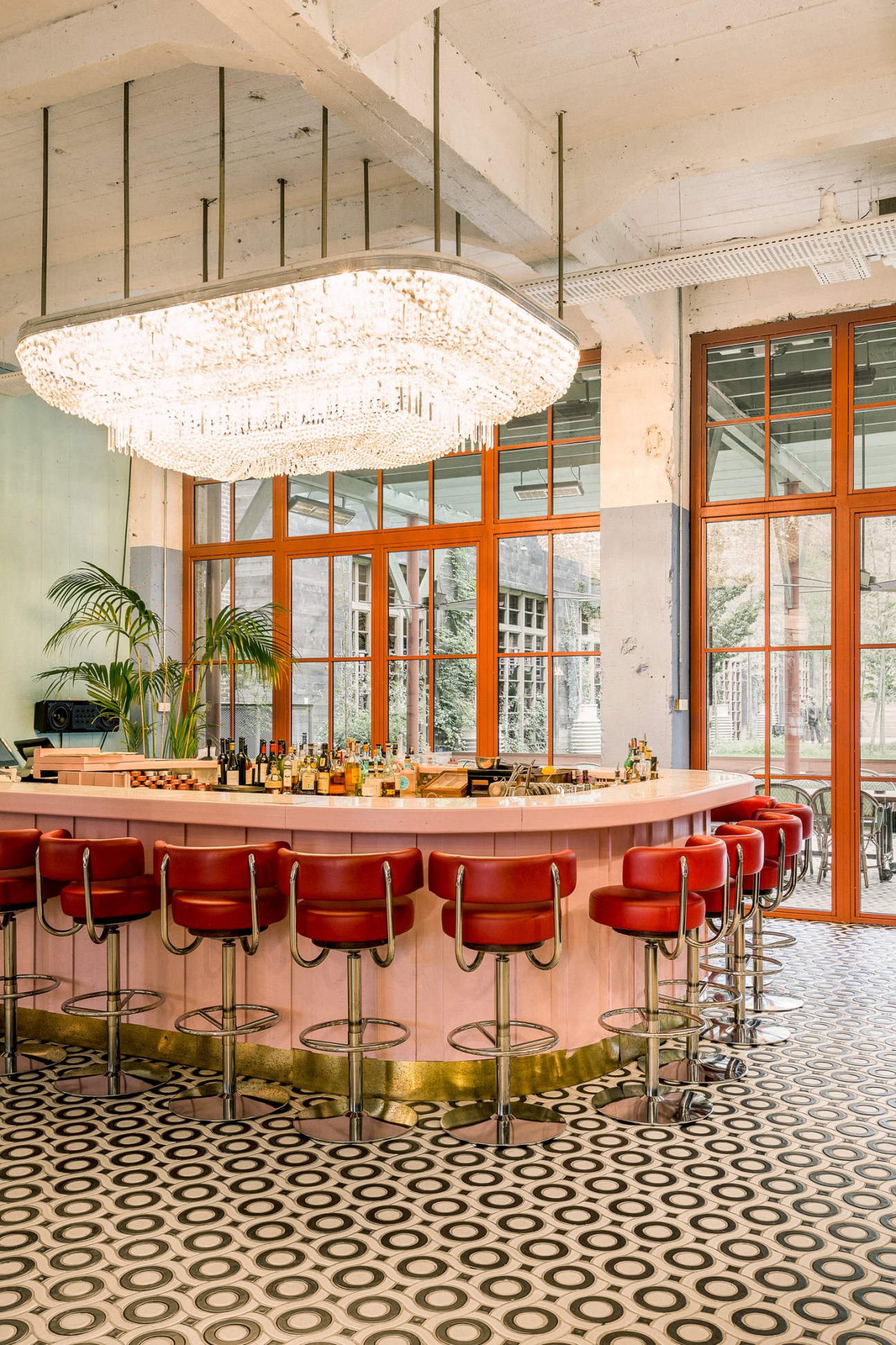 A curved pink bar counter with red upholstered stools and a crystal chandelier at Stamba Hotel in Tbilisi.