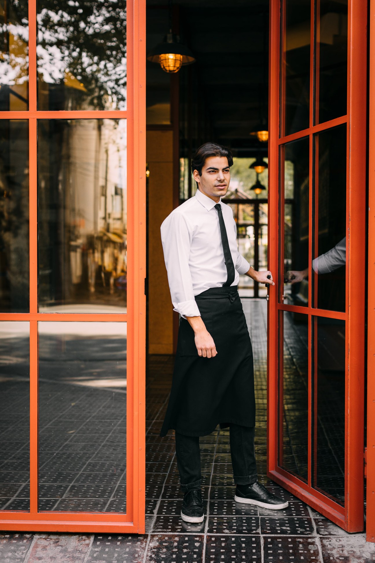 Man in white shirt and dark tie standing in doorway of Stamba Hotel with red-orange frame.
