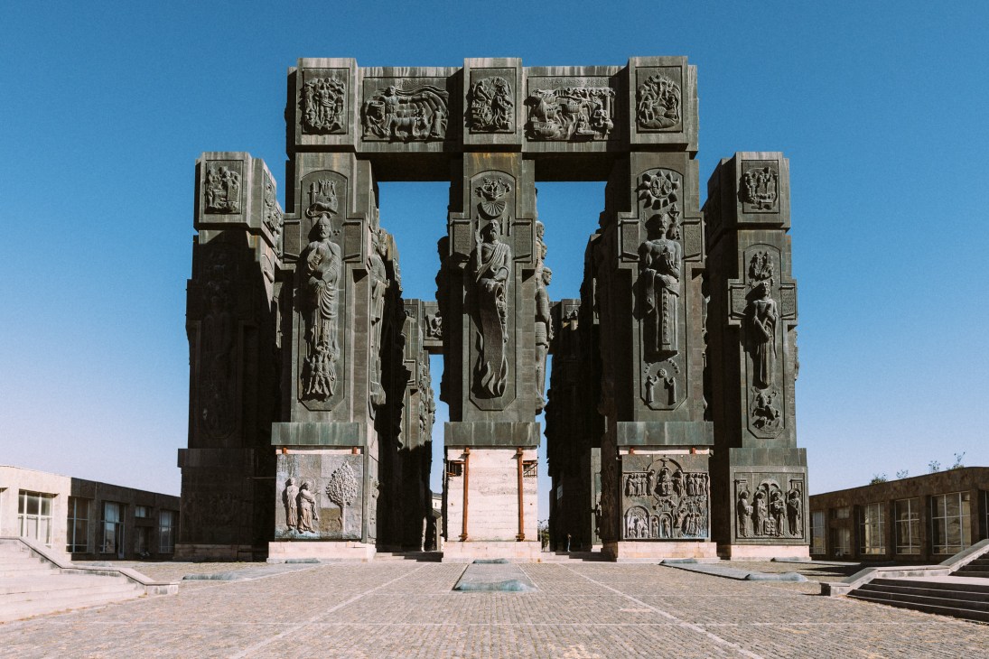 The Chronicle of Georgia monument features ornate stone columns with carved relief panels depicting historical scenes against a clear blue sky.