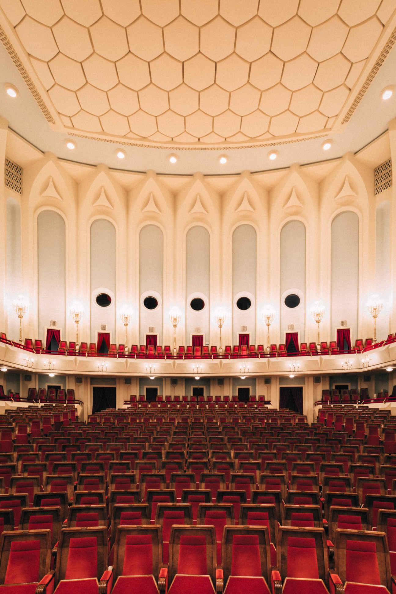 Interior of the Kakhidze Music Center auditorium with rows of red seats and ornate cream ceiling with geometric patterns.