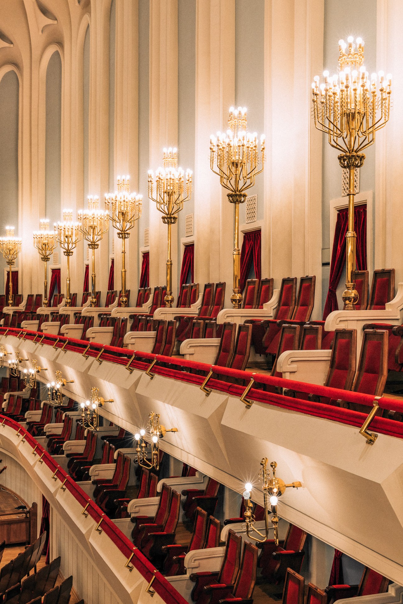 Interior of the Kakhidze Music Center concert hall with ornate brass candelabras and red velvet seats.