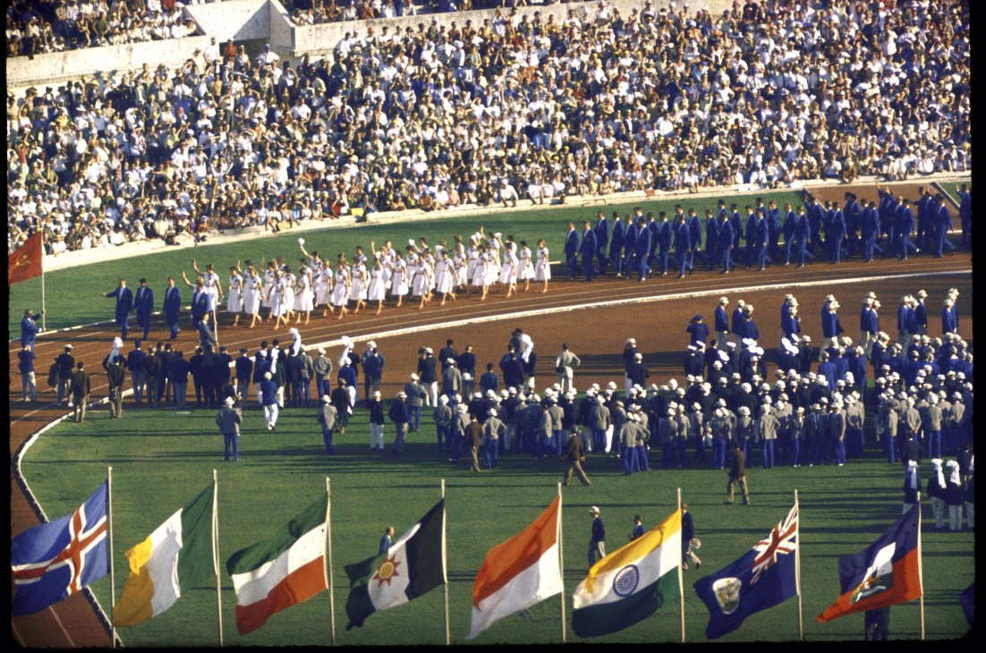 Opening ceremony of the 1960 Olympics with athletes parading on stadium field and international flags in foreground.