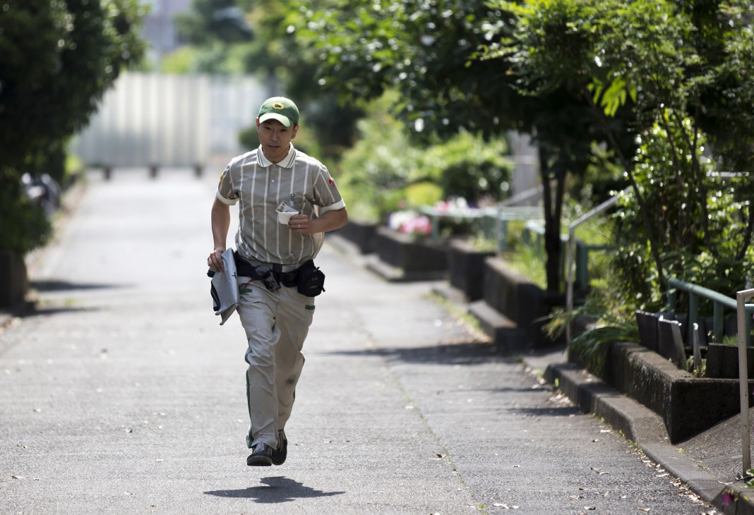 Yamato Transport delivery courier in striped uniform and cap running down a residential street with package in hand.